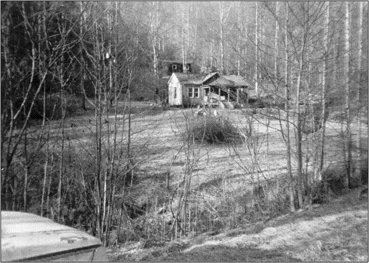 Black-and-white view of a small building in a wooded hollow.