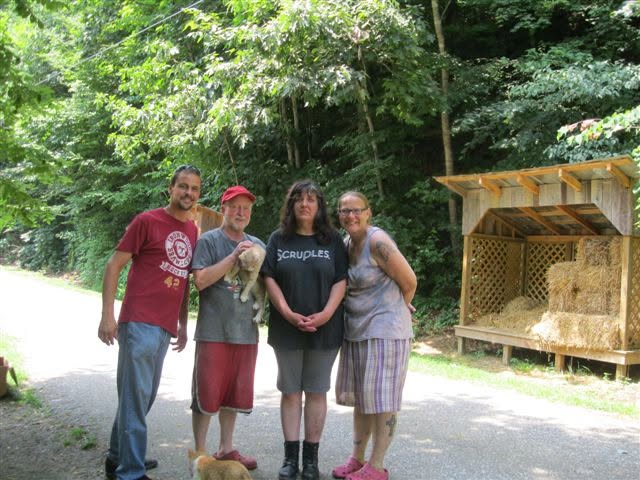 People gathered beside a sanctuary building and wooded road.
